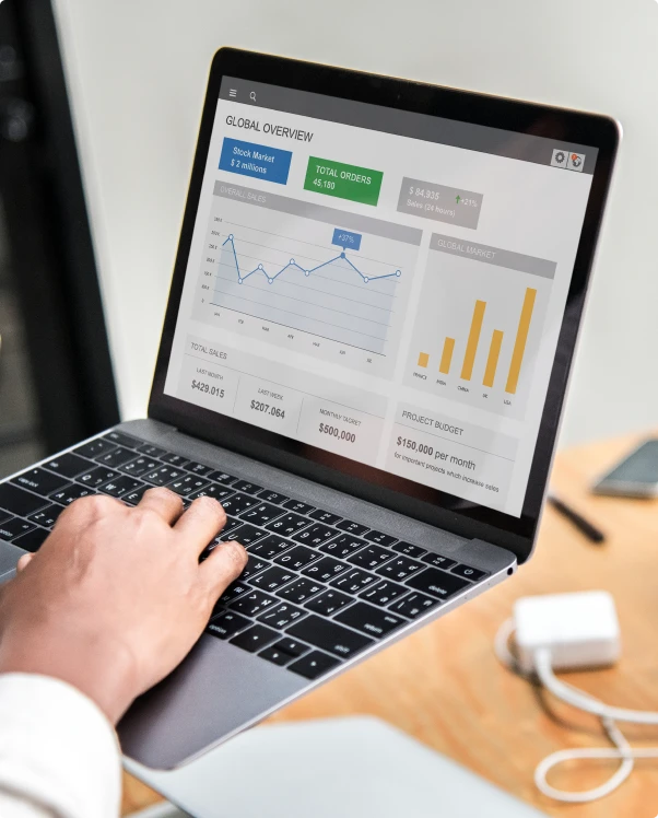 Hands on a laptop showing a sales dashboard with line and bar charts