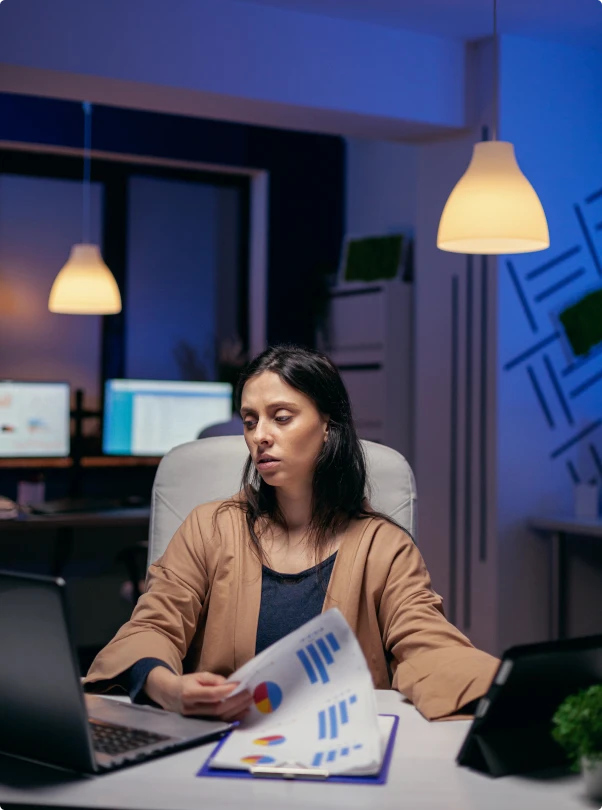 Woman reviewing printed charts at her desk in a dim office