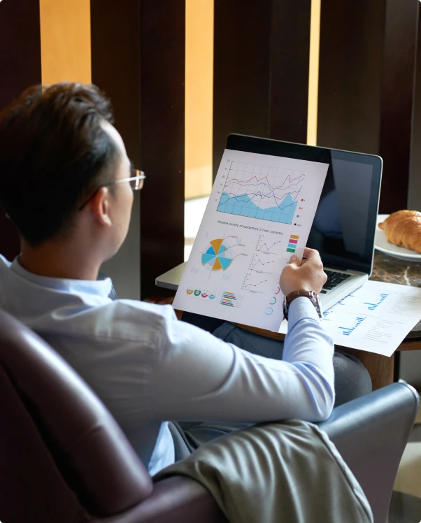 Man in glasses reviewing printed charts beside a laptop