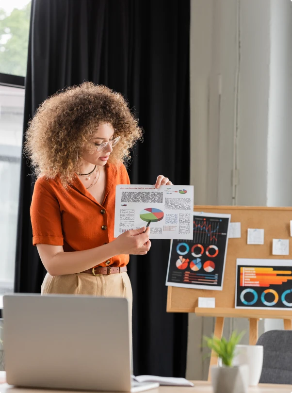 Marketer holding up a printed pie chart beside a laptop