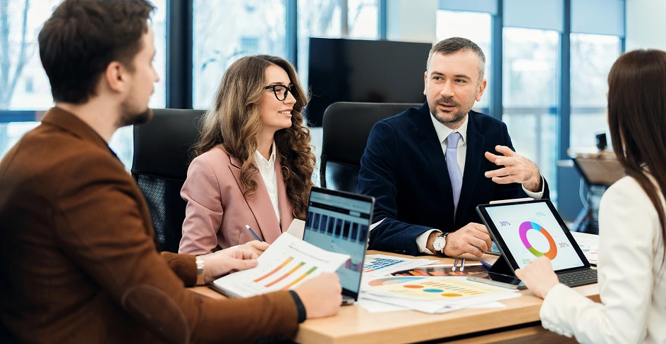 A team discussing reports at a meeting table with laptops and tablets