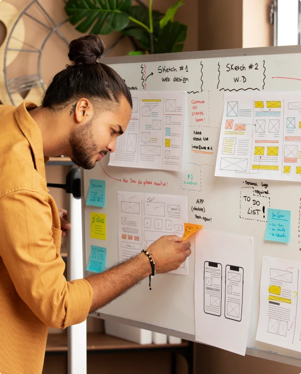 Designer pinning notes to a whiteboard covered in web page wireframe sketches