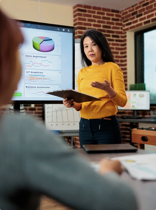Presenter in a yellow sweater walking a team through charts on a screen