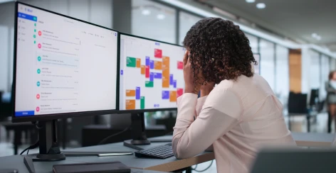 Frustrated woman resting her head on her hand in front of two monitors of data