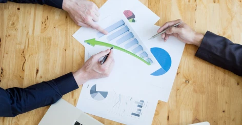 Two people marking up printed charts with a green arrow on a wooden desk