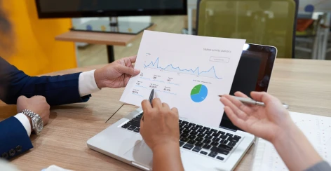 Hands reviewing a printed line chart report beside a laptop
