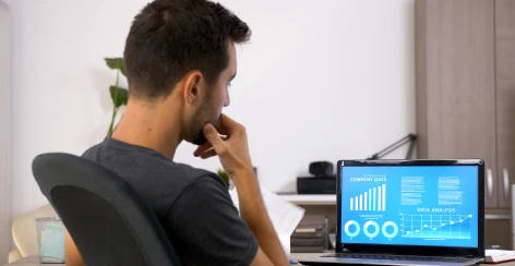 Man with his hand on his chin weighing a data dashboard on a laptop