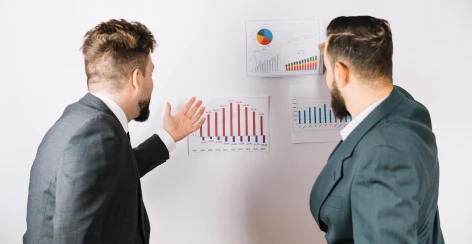 Two colleagues discussing bar charts pinned to a whiteboard