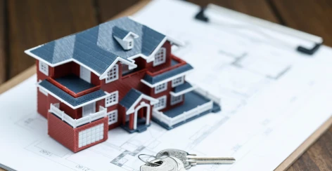 Model house resting on architectural floor plans with keys