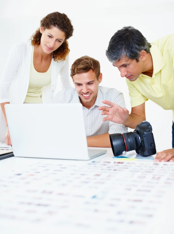 Three colleagues reviewing work on a laptop, with a camera on the desk