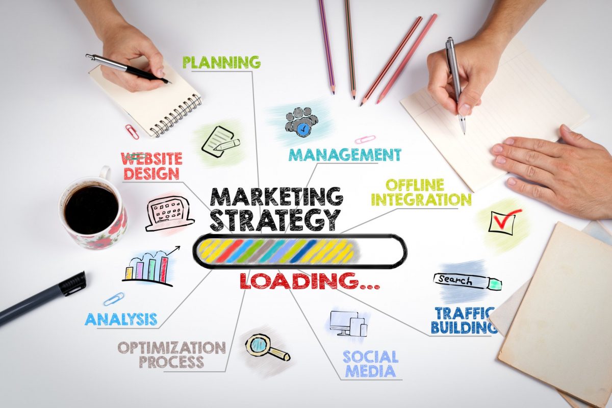 Image depicting marketing strategies with pencils, hands, a coffee, and paper on a desk.