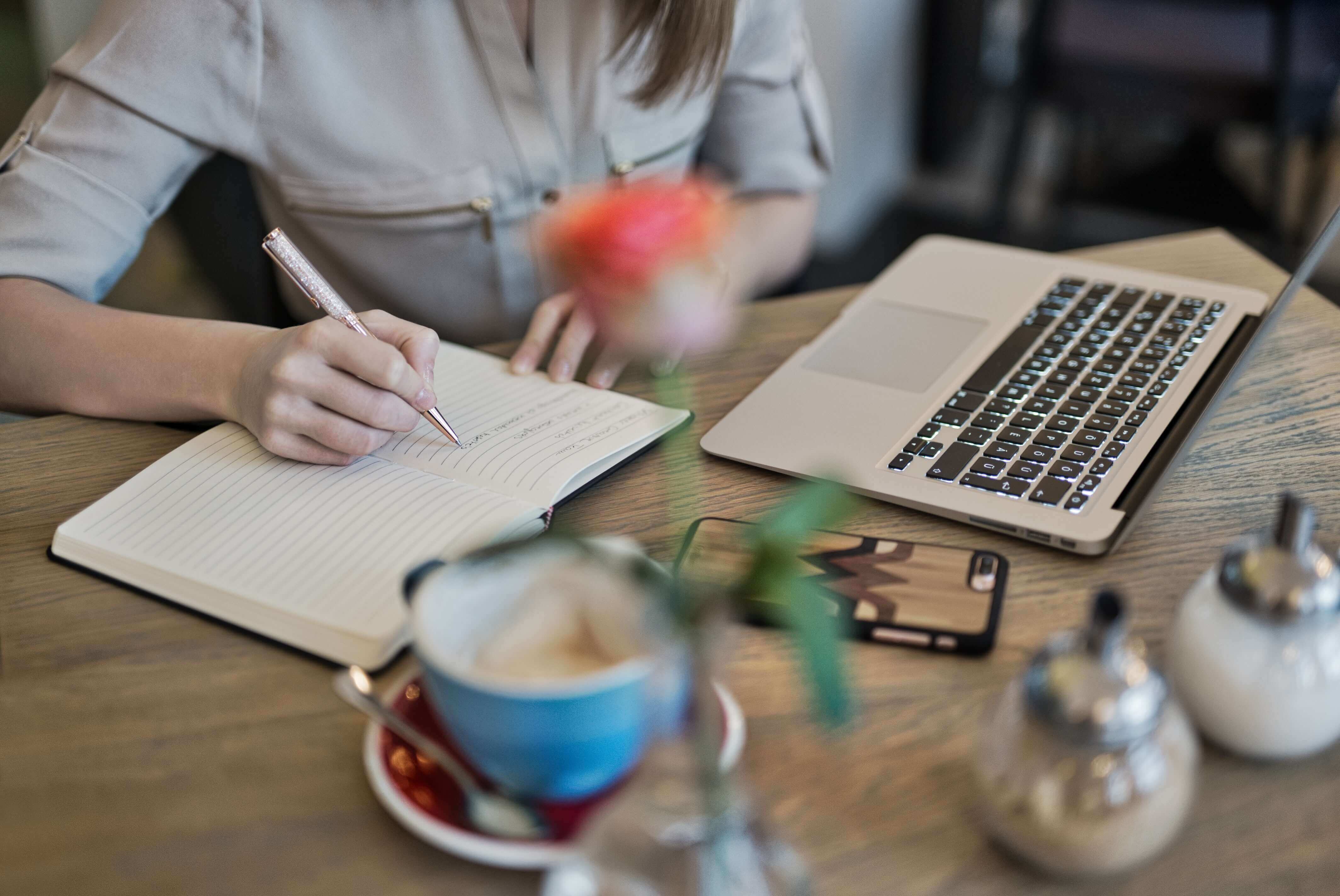 Woman in coffee shop writing her ideas in a notebook