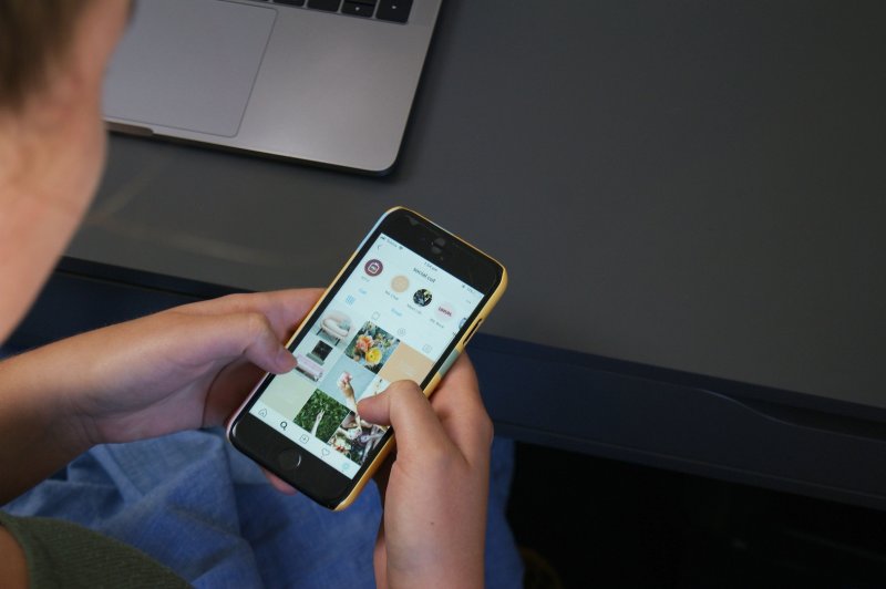 Young man holds iPhone and looks through Instagram Shopping on the screen.