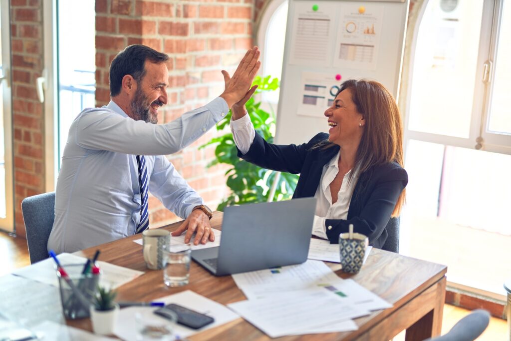 Male and female middle age business workers smiling happy and confident. Working together with smile on face hand giving high five at the office