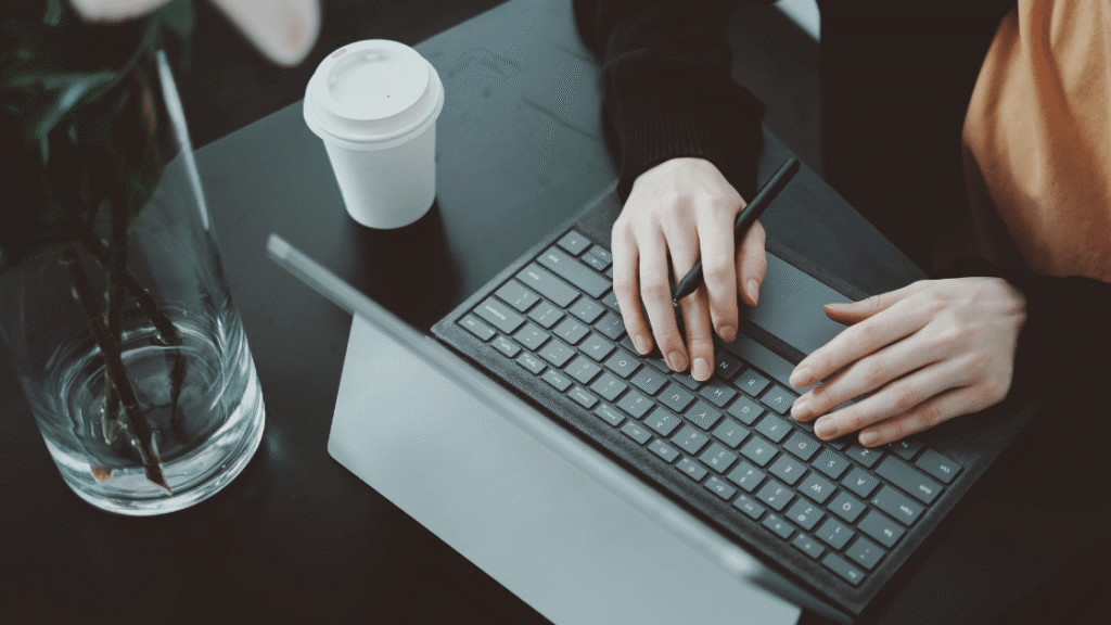 Generate Leads With Content Marketing - person typing on laptop with a takeaway coffee to their right