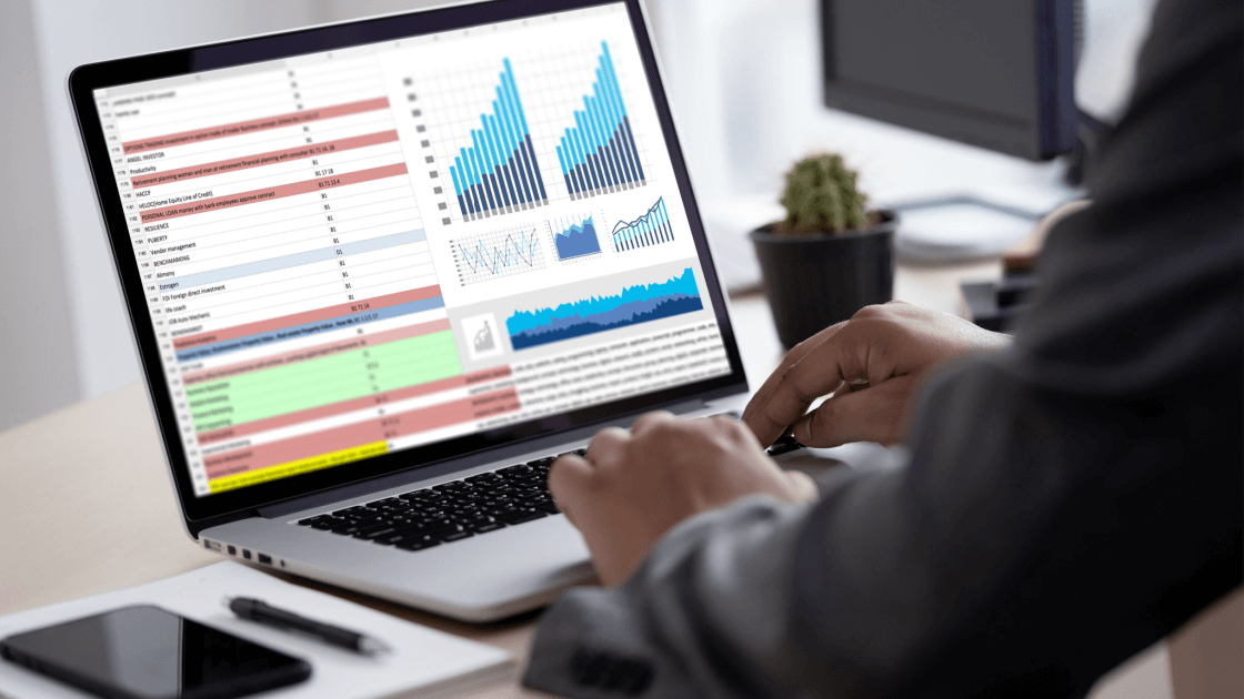 A person working on a laptop that shows a spreadsheet and bar charts