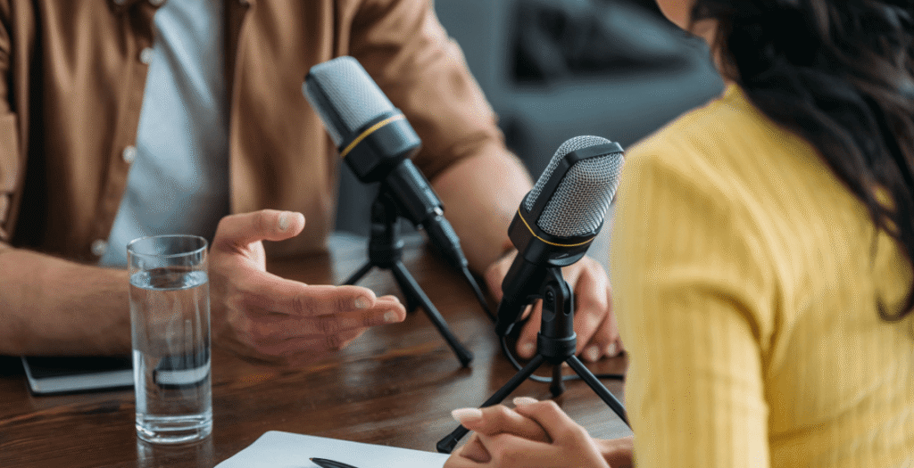 Two people interacting in front of two microphones on a podcast, an emerging digital marketing trend of 2023.