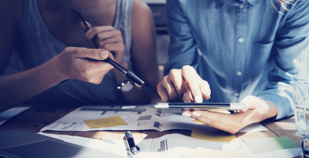 Two digital marketers reviewing performance strategy metrics on a tablet.