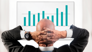 bald man sitting back with his hands on his back head looking at growth marketing bar graph with increases present