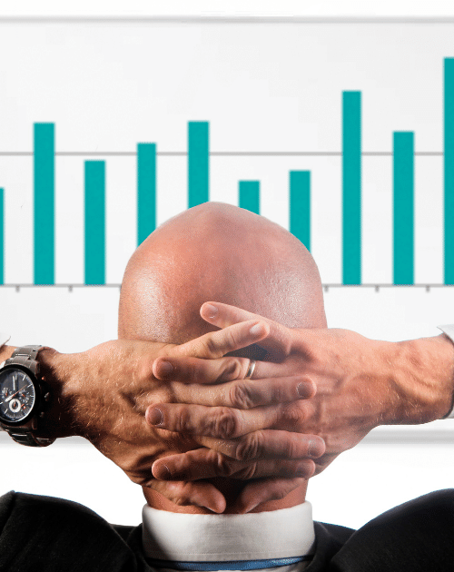 bald man sitting back with his hands on his back head looking at growth marketing bar graph with increases present